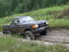 1990 Ford Bronco - A black 1990 Ford Bronco navigates a muddy, off-road trail surrounded by greenery.