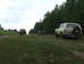 1990 Ford Bronco - Three off-road vehicles are parked on a dirt path surrounded by trees and grassy fields.