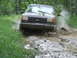 1990 Ford Bronco - A gray 1990 Ford Bronco navigates a muddy trail, kicking up water and dirt.