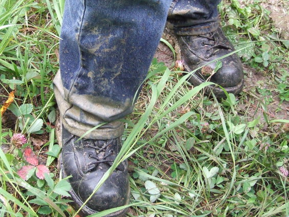 Muddy jeans and black boots on a person standing in grass and dirt