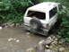 1990 Ford Bronco - A white Ford Bronco is partially submerged in a rocky stream, with trees and foliage surrounding it.