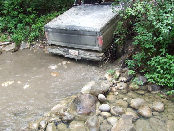 1990 Ford Bronco rear view, driving through shallow creek with rocky banks