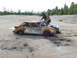 1990 Ford Bronco - A heavily damaged sedan, spray-painted with 'Burn Baby!', sits in a desolate area next to another vehicle.