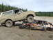 1990 Ford Bronco - A lifted Ford Bronco is parked on top of a heavily damaged and rusted car in a muddy outdoor area.