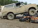1990 Ford Bronco - A muddy Ford Bronco is driven over a heavily damaged car in a wooded area.