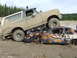 1990 Ford Bronco - A Ford Bronco is perched atop a heavily damaged car, both covered in mud and debris.