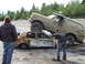 1990 Ford Bronco - A modified Ford Bronco is parked on top of a heavily damaged and burnt sedan, with two onlookers observing the scene.