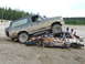 1990 Ford Bronco - A muddy 1990 Ford Bronco is parked on top of a heavily damaged car in a rural outdoor setting.