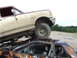 1990 Ford Bronco - A Ford Bronco is parked on top of a wrecked car in a junkyard.