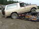 1990 Ford Bronco - A 1990 Ford Bronco is parked on top of a wrecked car in a dirt lot.