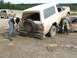 1990 Ford Bronco - Two people attempt to free a muddy 1990 Ford Bronco, with another vehicle visible in the background.