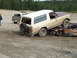 1990 Ford Bronco - A tan and maroon Ford Bronco is precariously perched on a pile of wrecked vehicles in a junkyard.
