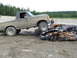 1990 Ford Bronco - A lifted pickup truck is positioned over two heavily damaged and burnt-out cars in a dirt lot.