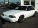 1991 Ford Mustang - A white 1991 Ford Mustang coupe is parked in front of a building, showing its front three-quarter view.