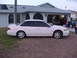 1994 Ford Taurus - A white sedan is parked in front of a house, with other vehicles visible in the driveway and garage.