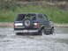 1990 Ford Bronco - A dark green 1990 Ford Bronco navigates through shallow water, kicking up spray.