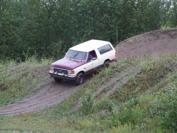Maroon and white Ford Bronco driving on a dirt hill. It's a 1987 model
