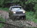 1990 Ford Bronco - This 1990 Ford Bronco navigates a rough, overgrown path, its headlights cutting through the dim forest light.