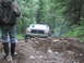 1990 Ford Bronco - A person in camouflage stands on a rough forest path as a Ford Bronco drives through mud and rocks.