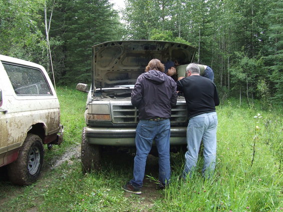 1990 Ford Bronco with hood open, people working on engine. Another Bronco parked to the left