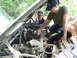 1990 Ford Bronco - People working on a vehicle's engine bay, with one person spraying something into the air intake.