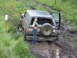 1990 Ford Bronco - A woman poses next to a muddy Ford Bronco that is stuck off-road.