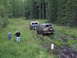 1990 Ford Bronco - Two vehicles navigate a muddy trail through a forest, with two people observing the scene.