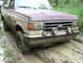 1990 Ford Bronco - A maroon and tan 1990 Ford Bronco navigates a muddy track, its front tires deep in the mire.