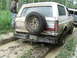 1990 Ford Bronco - A tan Ford Bronco navigates a muddy track in a wooded area, with another vehicle visible to the right.