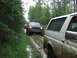 1990 Ford Bronco - A convoy of Ford Broncos navigates a muddy trail through a dense forest.