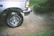 1995 Ford Bronco - The front quarter panel and tire of a silver Ford Bronco are visible on a wet driveway.
