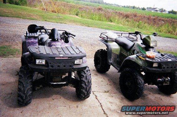 Two all-terrain vehicles parked on a concrete surface, with a grassy field in the background