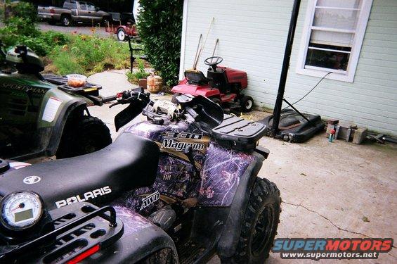 Two ATVs and a red lawnmower parked on a concrete driveway next to a house