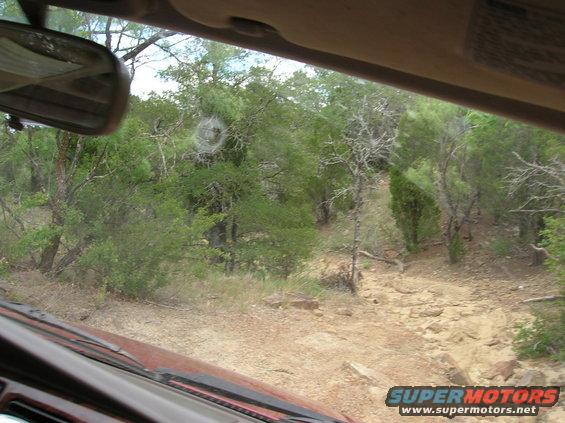 View from inside a vehicle looking out at a rocky, wooded trail