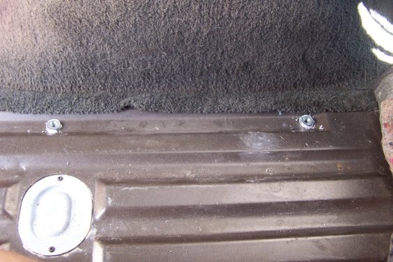 Close-up of the floor of a vehicle's cargo area showing two tie-down points and a circular access panel