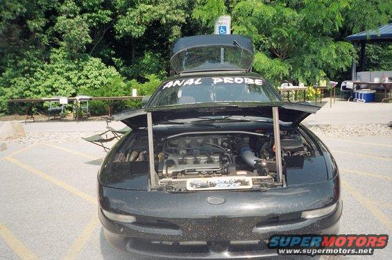 Black car with hood open, "ANAL PROBE" on windshield, engine visible