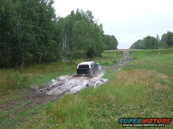 Rear view of black and white 1988 Ford Bronco driving through mud