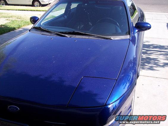Blue Ford Probe from the front-right, parked on a driveway. Another white car is visible in the background