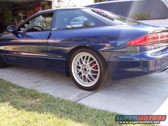 Blue 1995 Ford Probe GT coupe with aftermarket wheels and red brake calipers, seen from the rear three-quarter angle