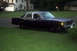 1989 Ford Crown Victoria LTD - A dark-colored sedan sits parked on a grassy lawn in front of a suburban home.