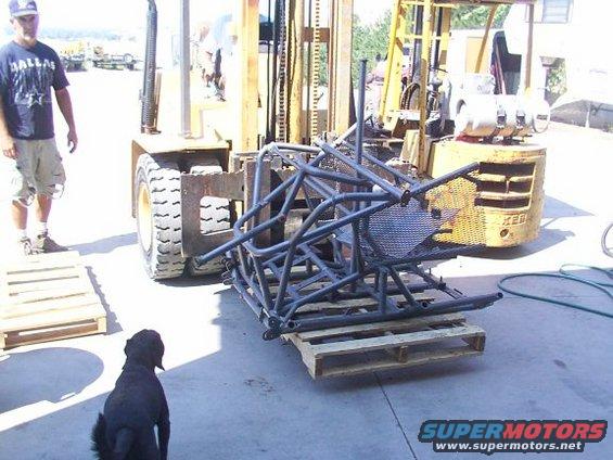 Roll cage assembly on wooden pallets, with a forklift and a man nearby