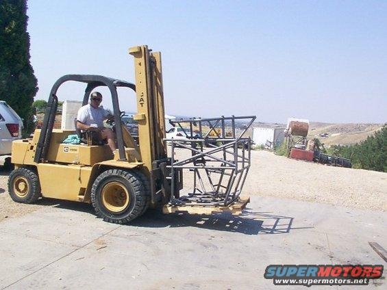 Yellow forklift with a man driving, carrying a metal frame on a pallet