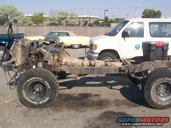 Truck chassis with engine and transmission removed, parked next to a van and a yellow car