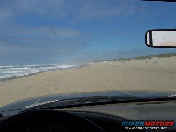 View from inside a vehicle driving on a sandy beach with ocean waves on the left