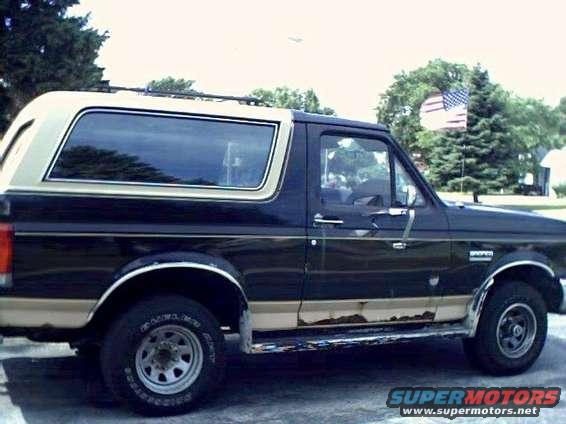 Side view of a 1989 Ford Bronco with tan trim and rust on the lower body panels