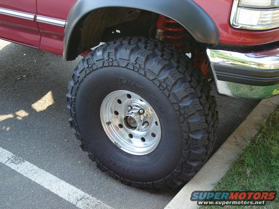 1994 Ford Bronco front wheel with aggressive tread tire and chrome rim, red body panel above