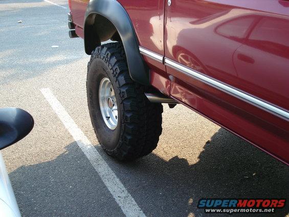 Side view of a red SUV's rear tire and fender flare. Chrome trim runs along the body