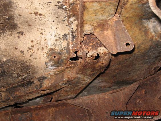 Close-up of heavily rusted frame rail with holes and a mounting bracket