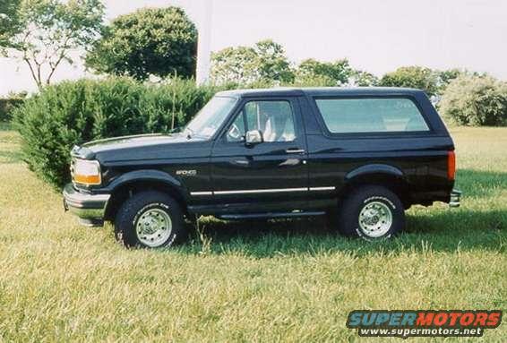 Black Ford Bronco parked on grass. Side view shows chrome wheels and tinted windows