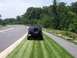 1996 Jeep Grand Cherokee - A black Jeep Grand Cherokee is parked on the grass beside a paved path and road, with a full-size spare tire on its rear.